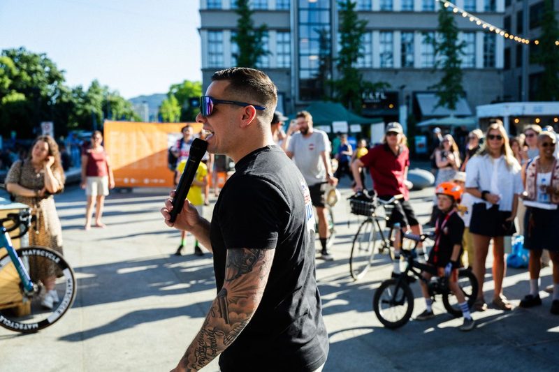 Raphael Walser moderiert mit Mikrofon einen Anlass auf einem Stadtplatz, im Hintergrund Publikum mit Velos
