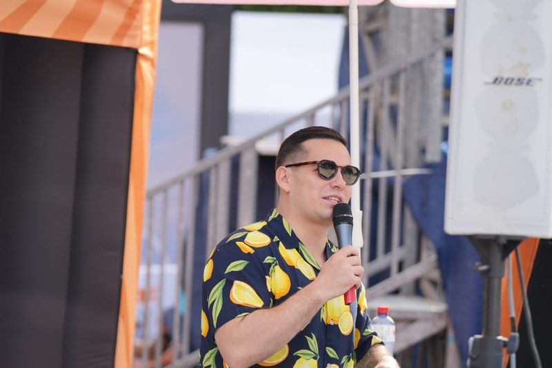 Raphael Walser spricht mit Mikrofon am Sportevent, im Hintergrund Tribüne und Sponsorenschirme