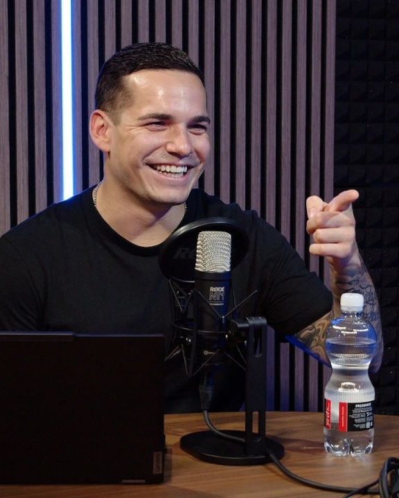 Raphael Walser lacht im Podcast-Studio, vor ihm das Mikrofon